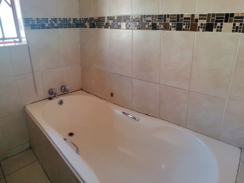 A functional bathroom featuring a built-in bathtub with chrome fixtures, complemented by neutral wall tiles and a decorative mosaic border.