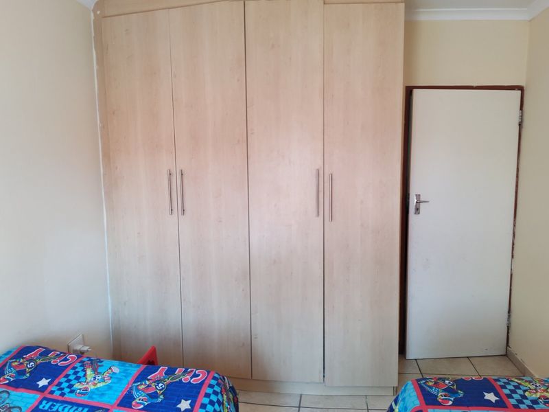 A bedroom featuring light wood-finish built-in wardrobes and tiled flooring, providing functional storage space.