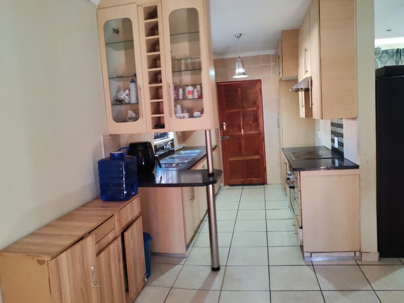 A functional kitchen featuring light wood cabinetry, dark laminate countertops, built-in appliances, and tiled flooring, leading to a rear exit door.