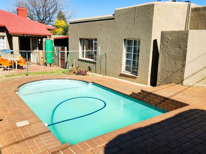Outdoor pool area featuring a swimming pool with brick paving surround, metal fencing, and access to the main house and adjacent structure.