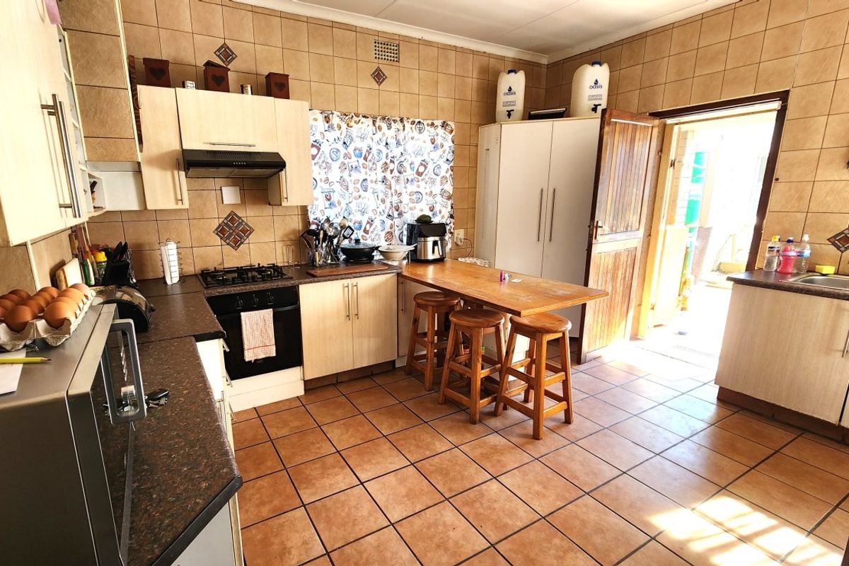 A functional kitchen featuring tiled walls and flooring, built-in cabinetry, a gas hob with extractor, and direct access to the exterior.