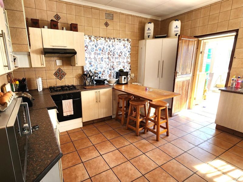 A functional kitchen featuring tiled walls and flooring, built-in cabinetry, a gas hob with extractor, and direct access to the exterior.