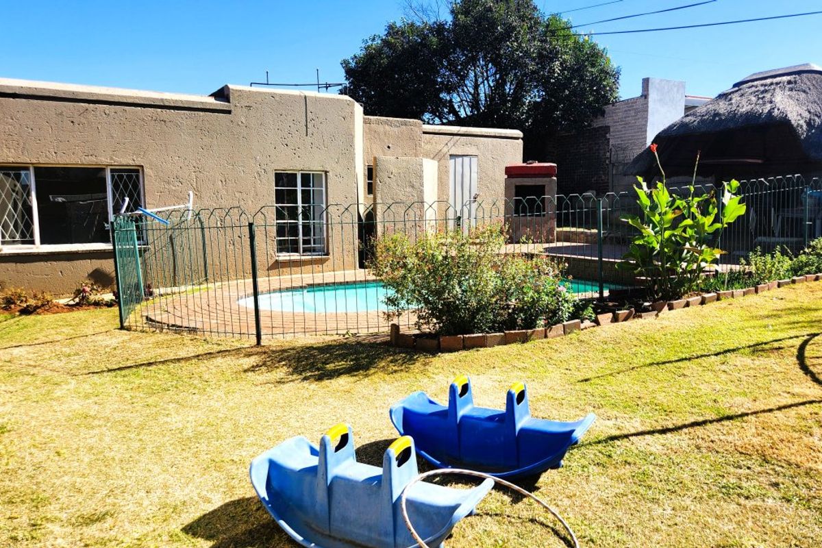 Rear garden area featuring a swimming pool, paved surround, built-in braai, and a thatched lapa structure.