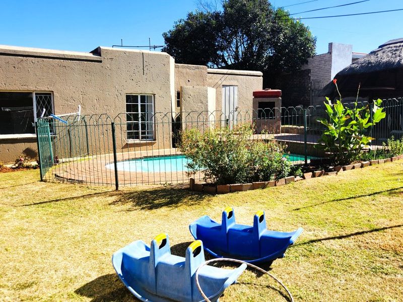 Rear garden area featuring a swimming pool, paved surround, built-in braai, and a thatched lapa structure.
