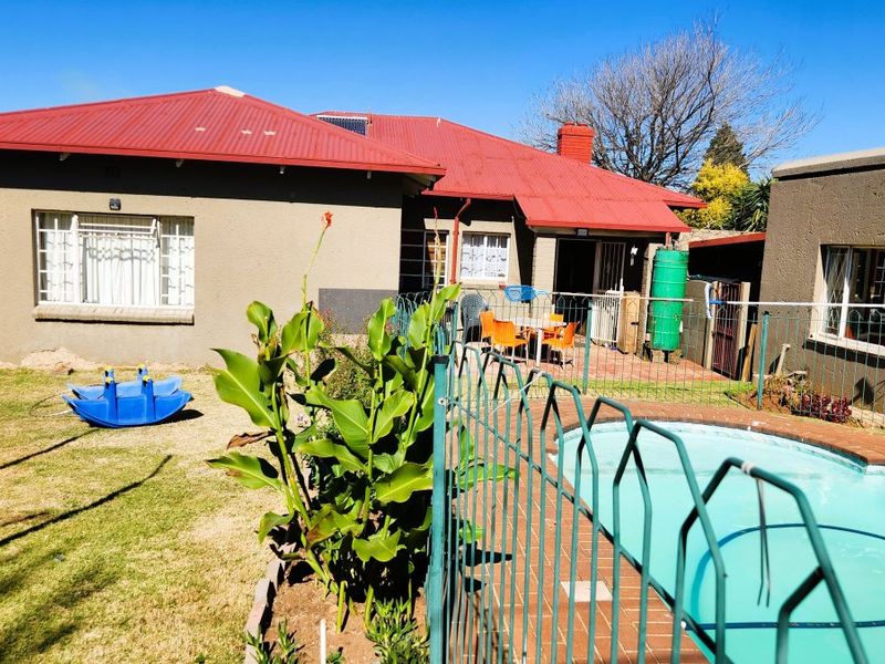 Rear view of the property featuring a swimming pool with safety fencing, a paved patio area, and a corrugated metal roof.