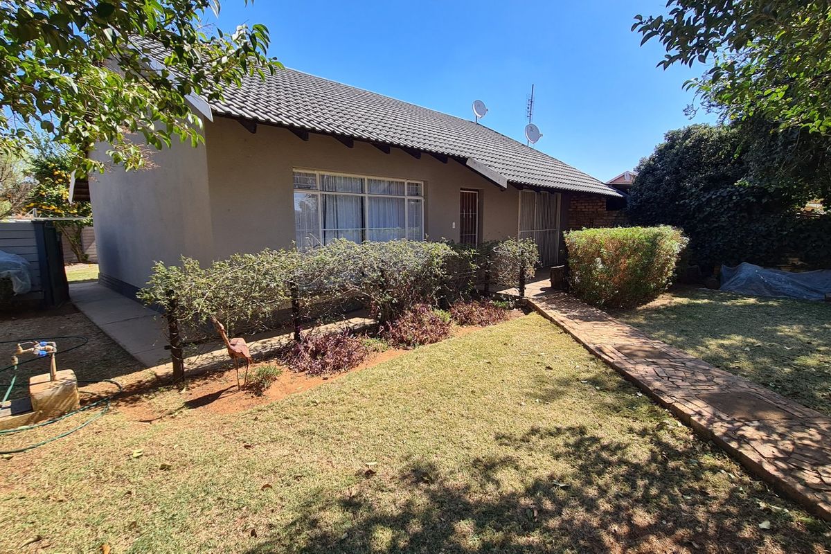 Rear view of the townhouse featuring a tiled roof, paved walkway, and established garden area with security access points.