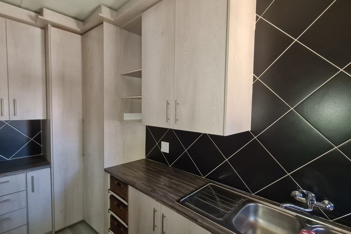 A clean, modern kitchen featuring light wood-grain cabinetry, dark tiled backsplash, and a stainless steel sink with a mixer tap.
