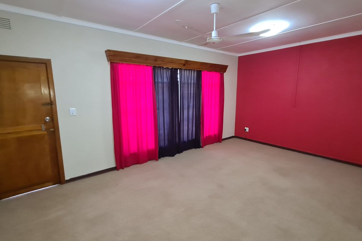 A spacious, empty living room featuring neutral carpet flooring, a ceiling fan, and a prominent red accent wall.
