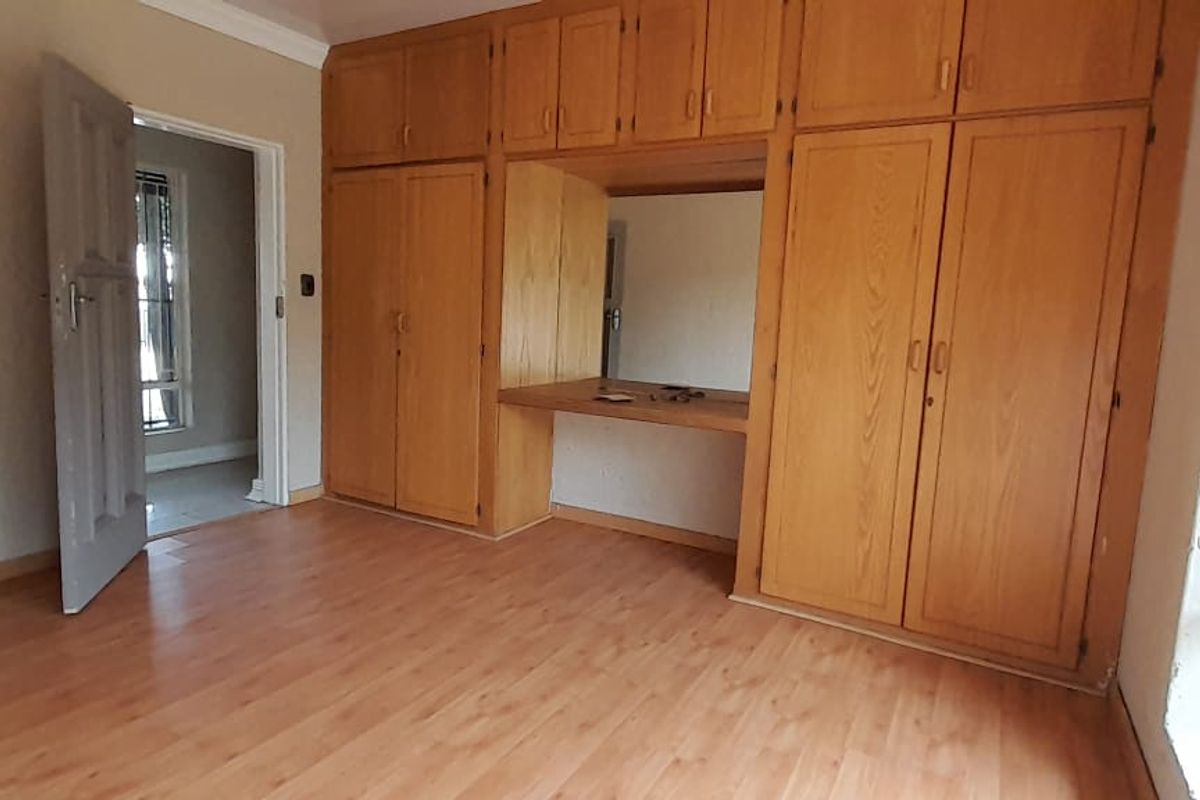 A vacant bedroom featuring extensive built-in wooden cabinetry, a vanity area, and laminate flooring, secured with window bars.