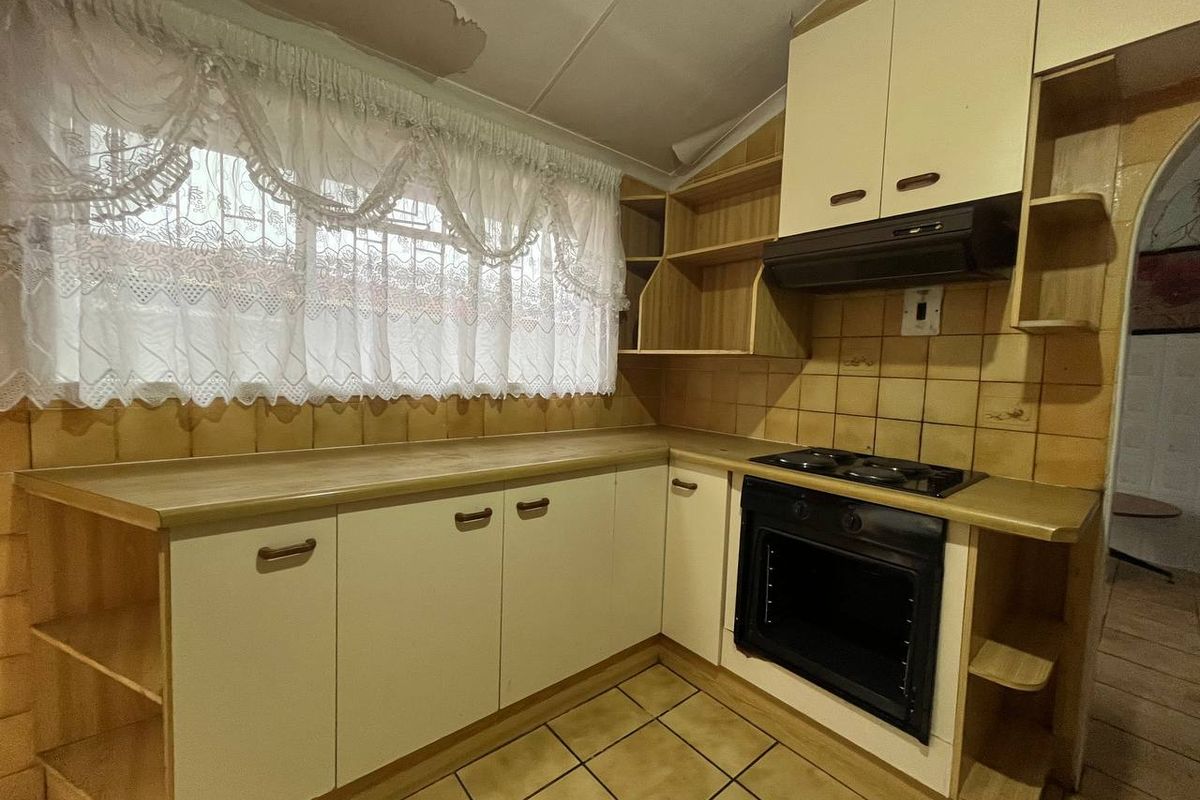 A dated kitchen featuring built-in cabinetry, an integrated oven and hob, and tiled finishes, currently showing signs of ceiling water damage and wear.