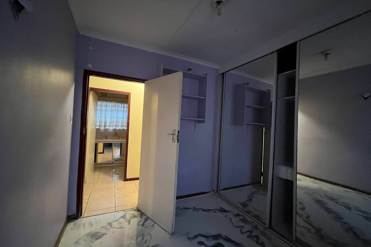 An empty bedroom featuring built-in mirrored wardrobes, integrated shelving, and tiled flooring, with an adjacent view into a bathroom area.