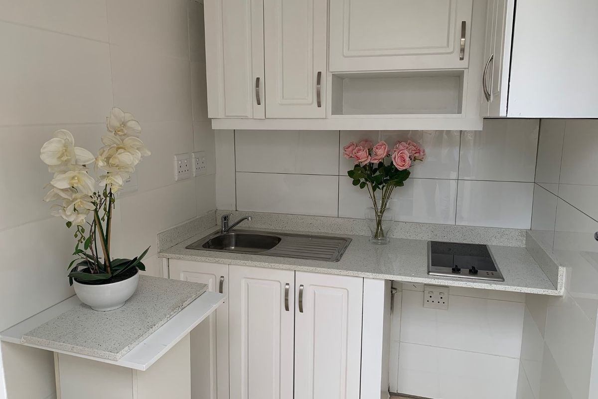 Compact kitchen featuring white built-in cabinetry, stone countertops, a stainless steel sink, and a built-in electric hob with tiled backsplash.