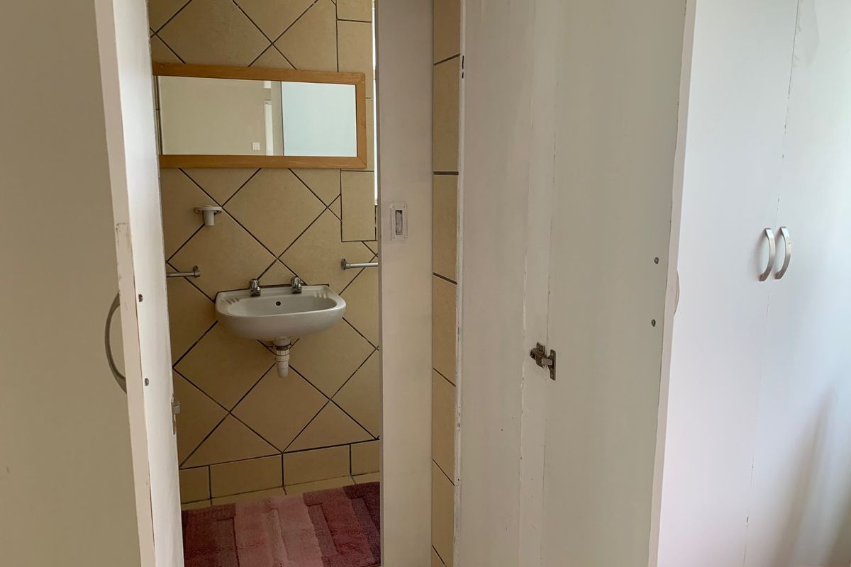 A compact bathroom featuring a wall-mounted basin with tiled splashback and adjacent built-in storage cabinetry.