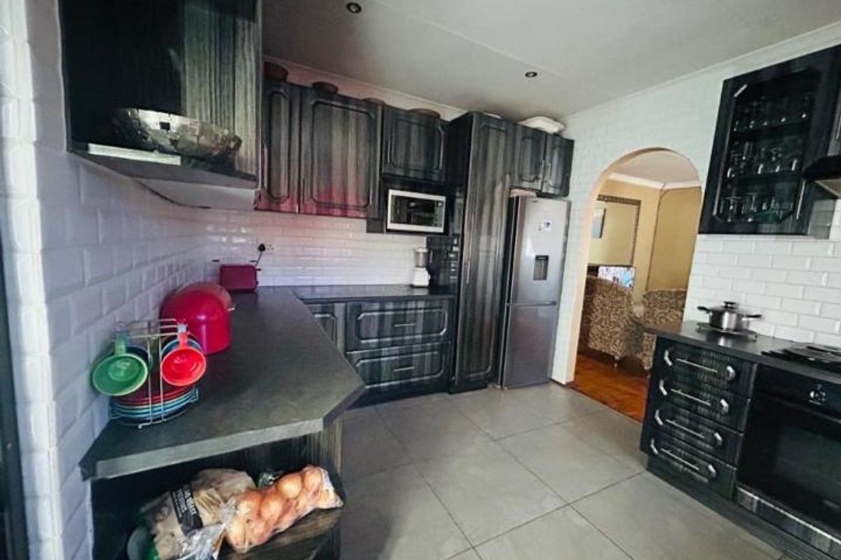 A functional kitchen featuring dark wood-look cabinetry, subway tile backsplash, built-in oven, and microwave, with tiled flooring and an arched entryway to the living area.