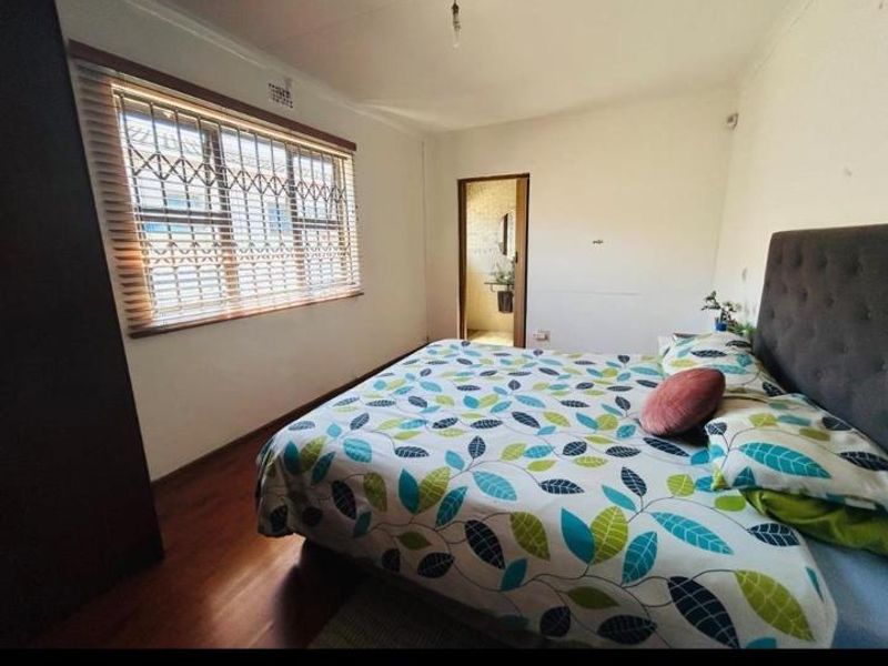 A functional bedroom featuring laminate flooring, built-in wardrobe storage, and a window fitted with security bars and venetian blinds.