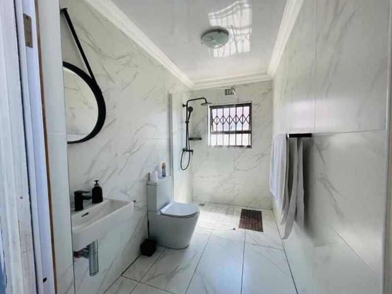 Modern bathroom featuring floor-to-ceiling marble-look tiles, a wall-mounted basin, toilet, and a walk-in shower area with a security gate on the window.
