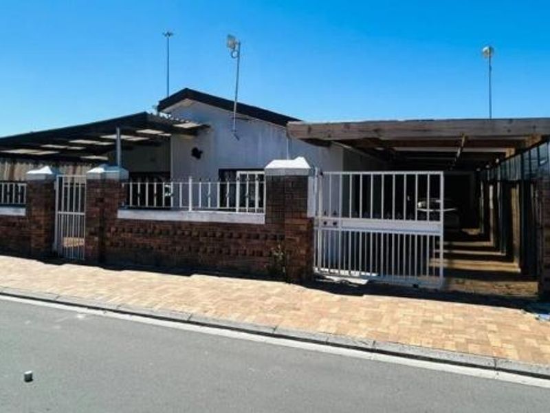 Front elevation of a residential property featuring a brick boundary wall, metal security gate, and a covered carport area.