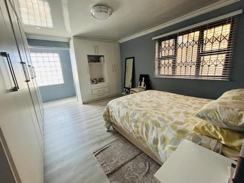 A well-maintained bedroom featuring extensive built-in cabinetry, laminate flooring, and a glass block window providing natural light.