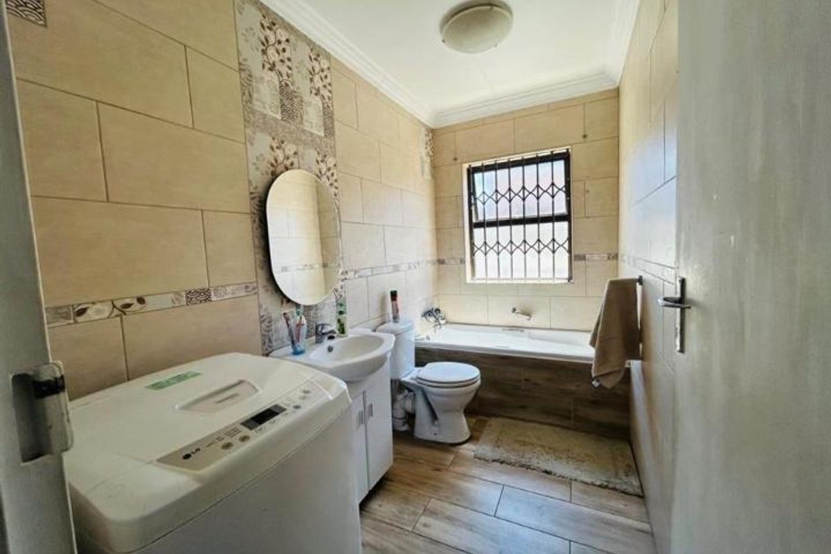 A functional bathroom featuring a built-in bathtub, pedestal washbasin, toilet, and tiled finishes with security bars on the window.