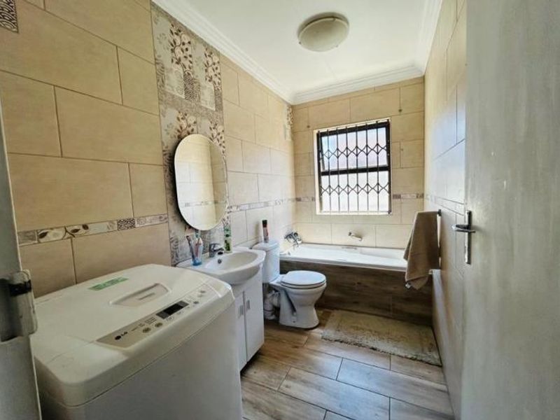 A functional bathroom featuring a built-in bathtub, pedestal washbasin, toilet, and tiled finishes with security bars on the window.