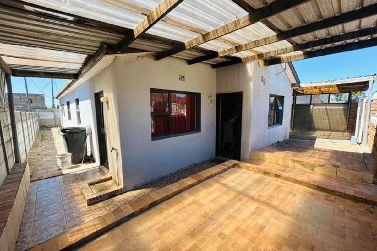 Rear exterior view featuring a covered patio area with brick paving, corrugated roofing, and access to the side yard.