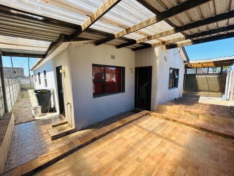 Rear exterior view featuring a covered patio area with brick paving, corrugated roofing, and access to the side yard.