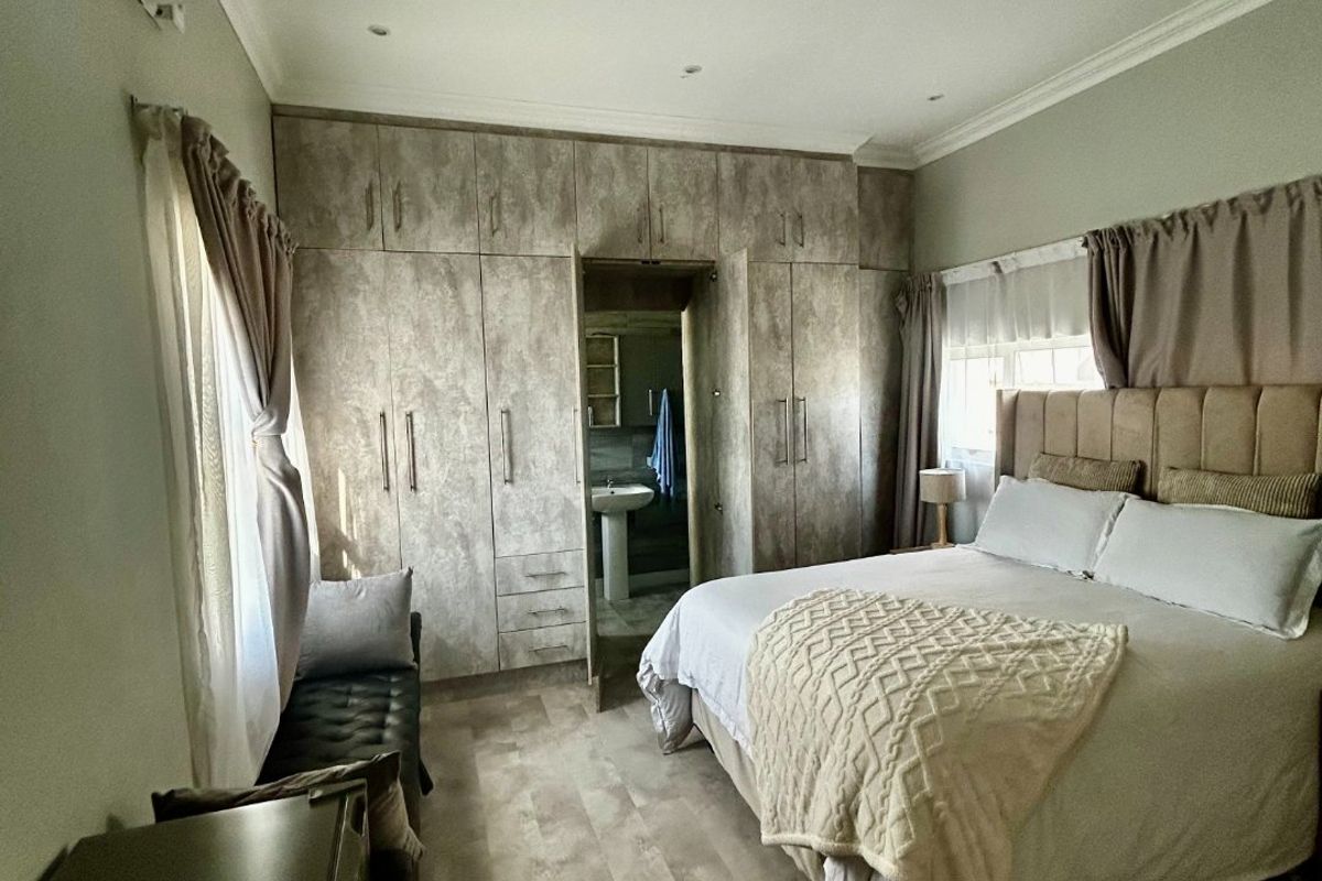 Spacious bedroom featuring extensive built-in cupboards, laminate flooring, recessed lighting, and an integrated air conditioning unit with direct access to an en-suite bathroom.