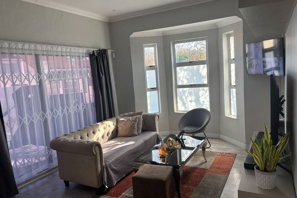 A bright living room featuring a large bay window, recessed lighting, and a sliding glass door with security gate access to the exterior.