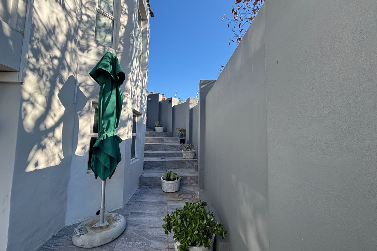 A paved side walkway featuring stone tiling, concrete boundary walls, and an external staircase leading to the rear of the property.