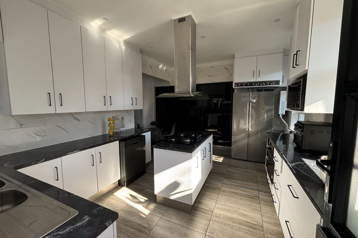 Modern kitchen featuring a central island with gas hob, sleek white cabinetry, stone countertops, marble-look splashbacks, and integrated stainless steel appliances.