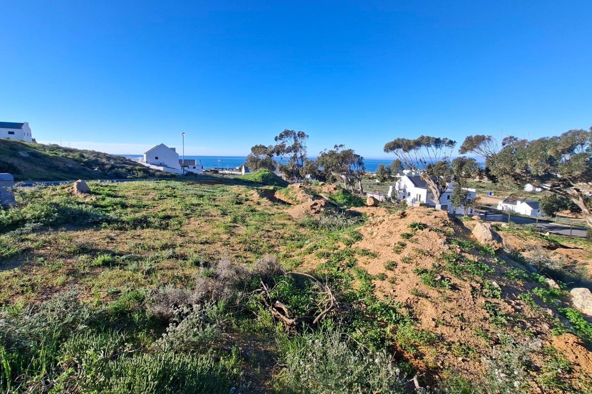 A wide-angle view of a vacant residential plot featuring natural coastal terrain and distant ocean views.