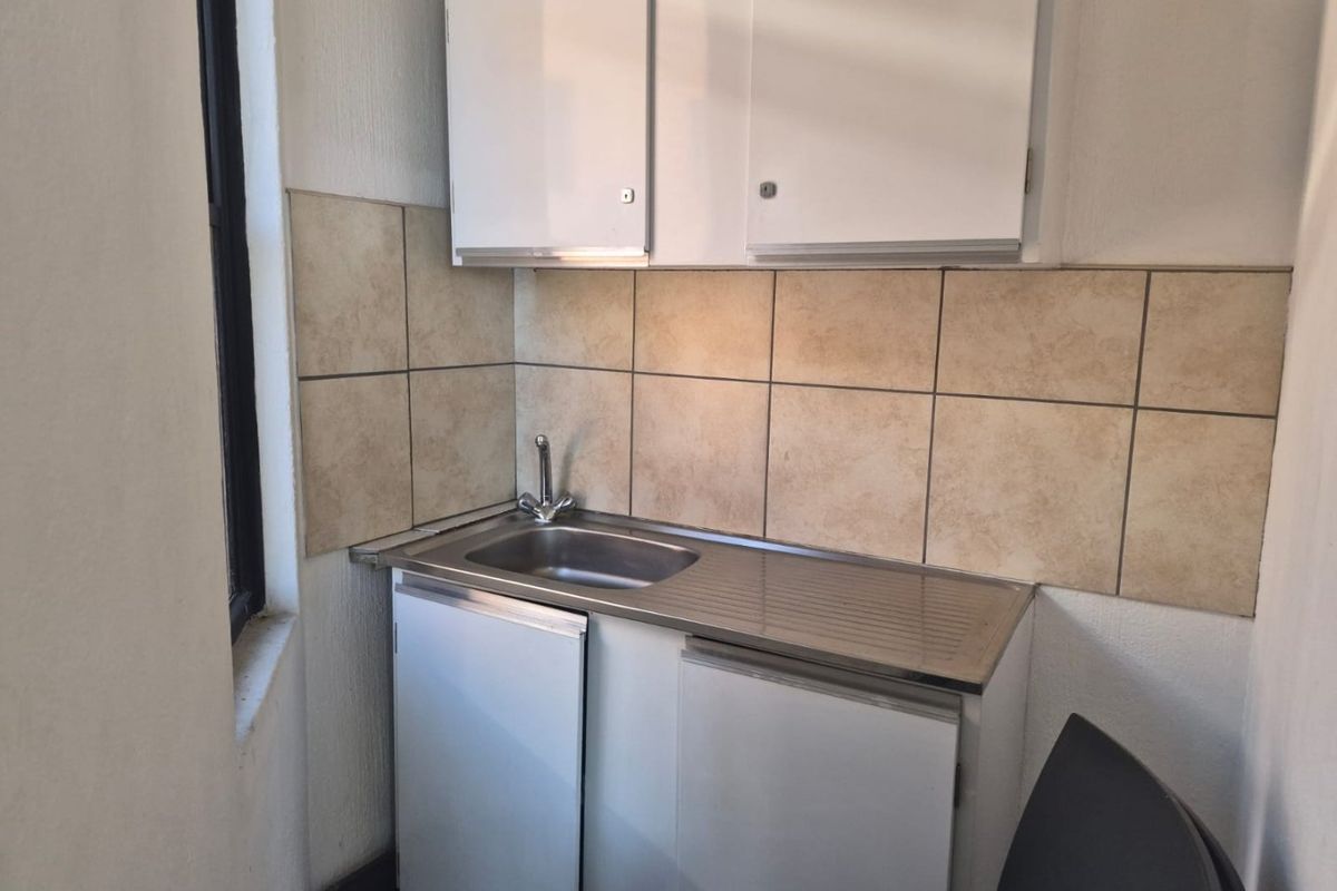 A compact kitchenette featuring a stainless steel sink, tiled backsplash, and basic upper and lower cabinetry.
