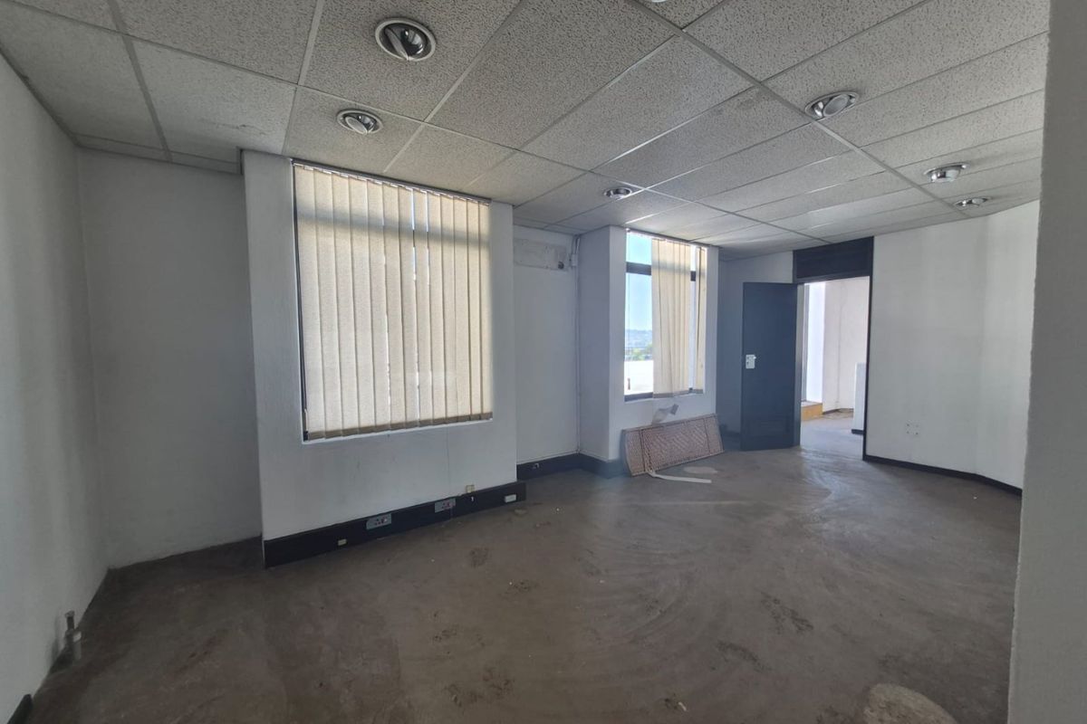 An empty commercial office space featuring a suspended ceiling with recessed lighting, vertical blinds, and exposed flooring ready for refurbishment.