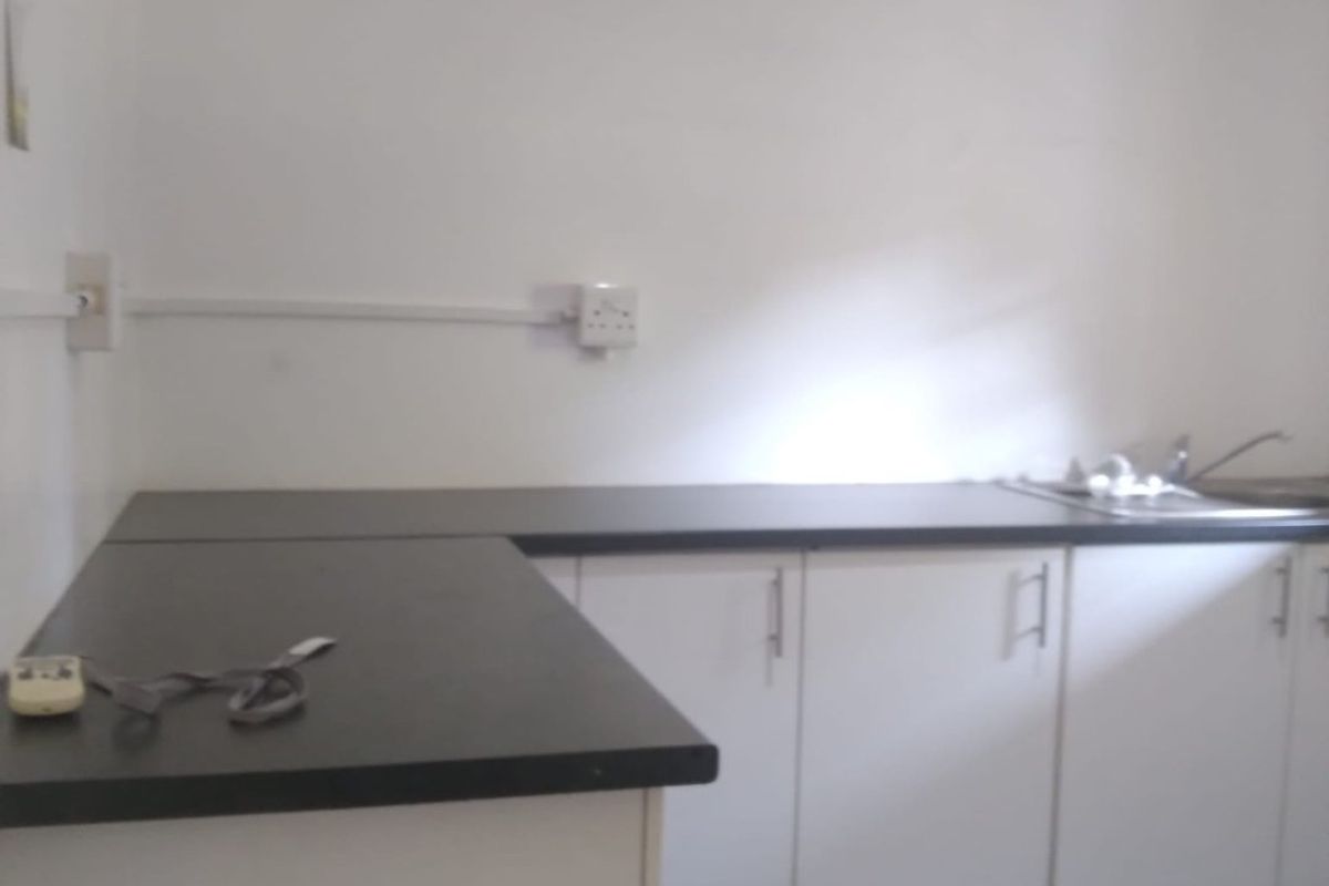 A functional kitchen area featuring white base cabinetry, dark laminate countertops, a stainless steel sink, and tiled flooring.