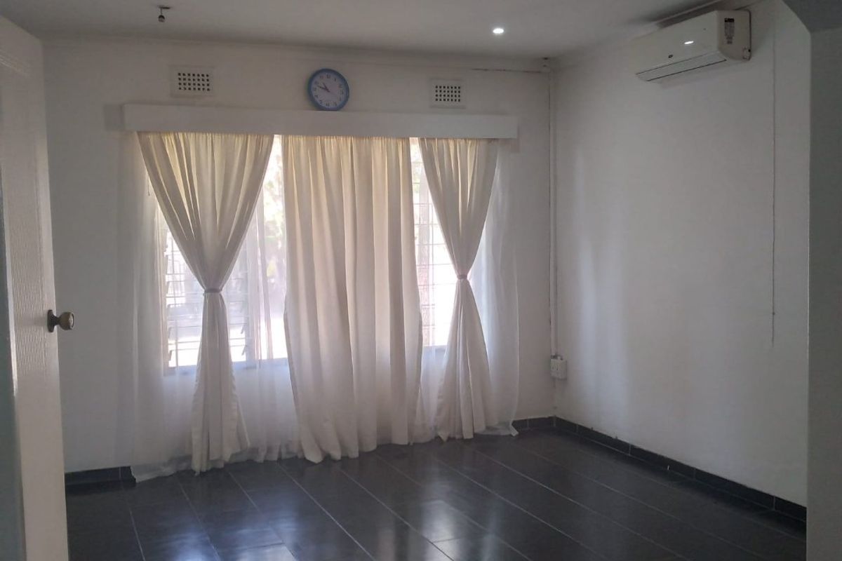 An empty living room featuring dark tiled flooring, an archway entrance, recessed lighting, and a wall-mounted air conditioning unit.