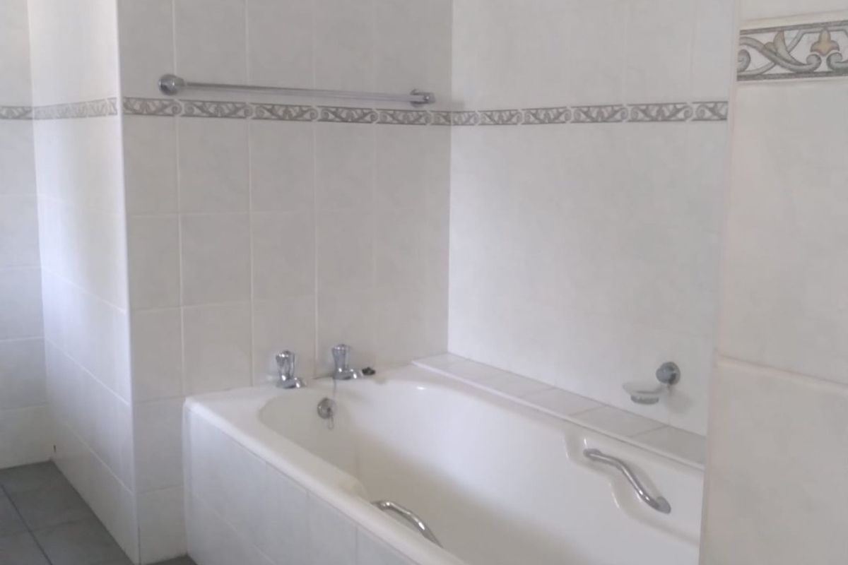 A clean, functional bathroom featuring a built-in bathtub with tiled surround and neutral wall tiling.