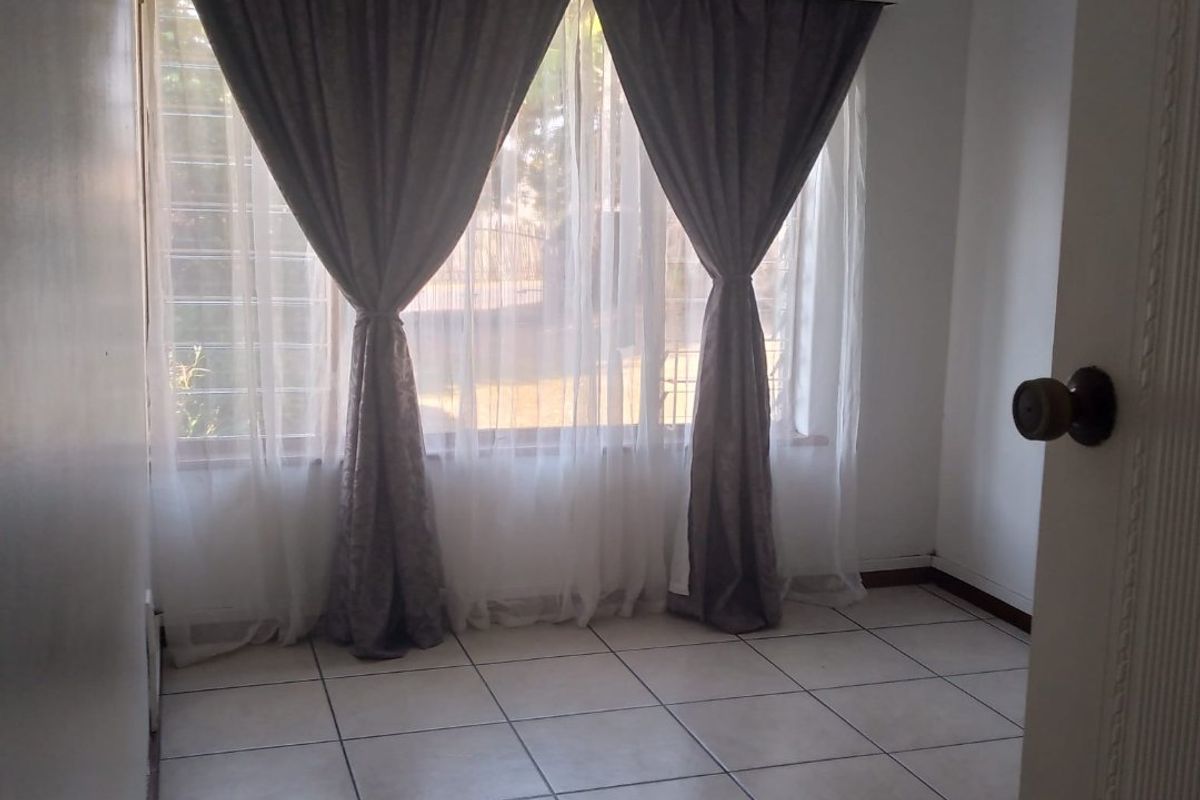 An empty bedroom featuring tiled flooring, a curtain pelmet, and security bars on the window, providing a blank canvas for potential interior design.