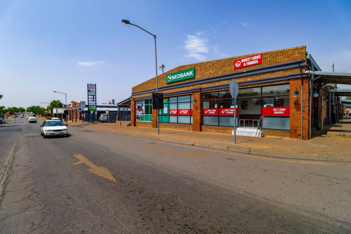 Street-level view of a commercial building featuring a brick facade, large glass storefront windows, and prominent signage along a public road.