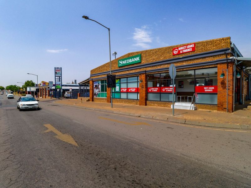 Street-level view of a commercial building featuring a brick facade, large glass storefront windows, and prominent signage along a public road.