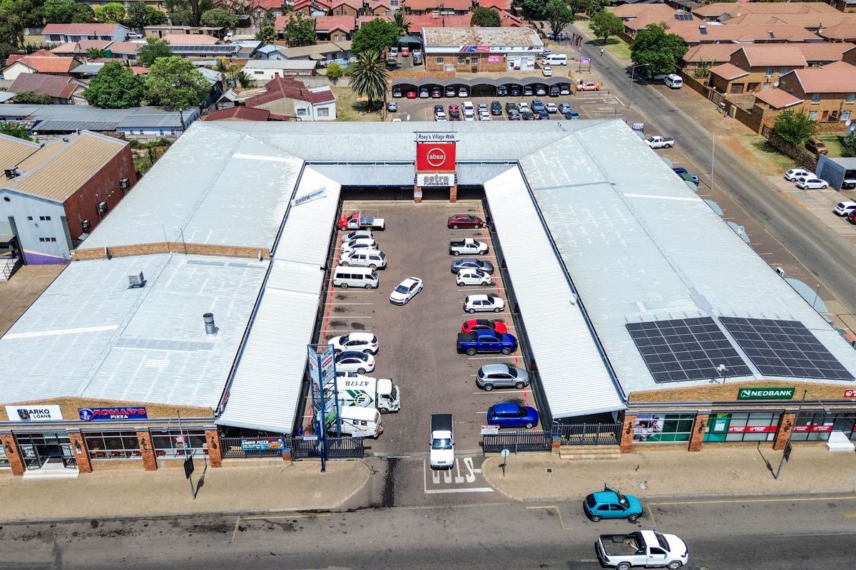 Aerial view of a commercial shopping center featuring a central parking courtyard, metal roofing, and integrated solar panels.