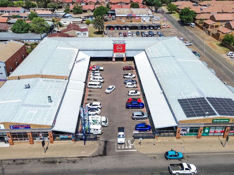 Aerial view of a commercial shopping center featuring a central parking courtyard, metal roofing, and integrated solar panels.