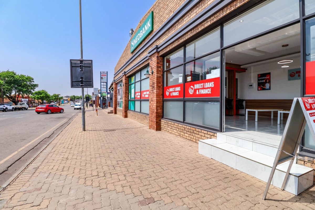 Street-level view of a commercial storefront featuring a brick facade, large display windows, and paved sidewalk access.