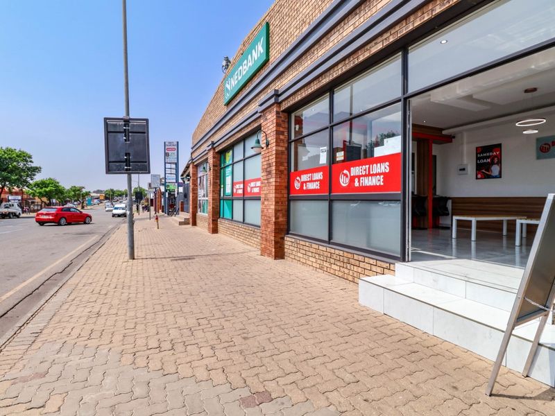 Street-level view of a commercial storefront featuring a brick facade, large display windows, and paved sidewalk access.