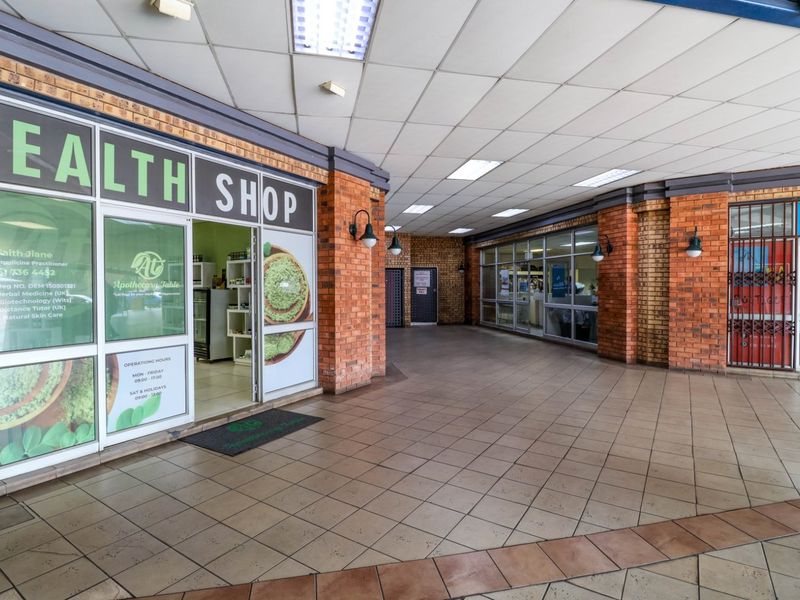 Commercial storefront entrance featuring exposed brickwork, tiled walkway, and glass display windows within a covered shopping arcade.