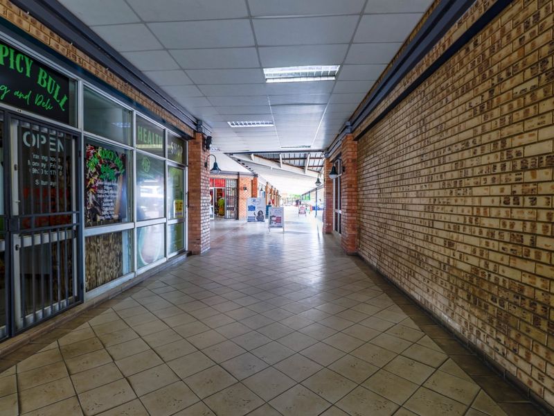A well-maintained commercial shopping center walkway featuring tiled floors, exposed brick walls, and glass storefronts under a suspended ceiling.