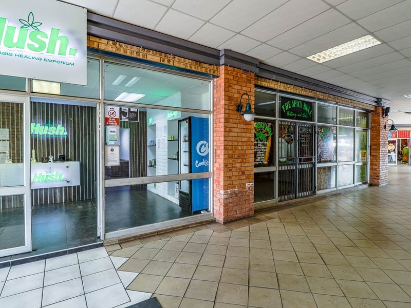 Commercial storefronts featuring glass facades, brick detailing, and tiled flooring located within a covered shopping arcade.