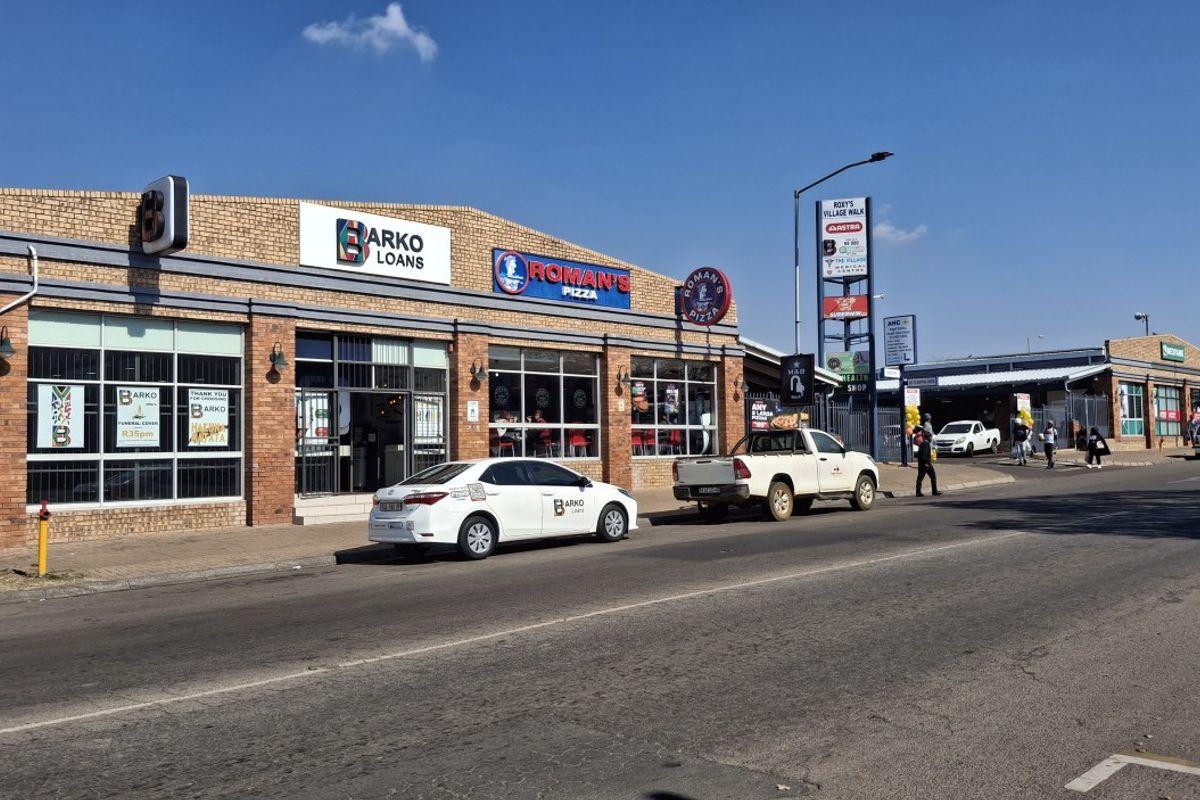 Street-level view of a commercial retail strip center featuring face brick construction, large display windows, and prominent tenant signage.