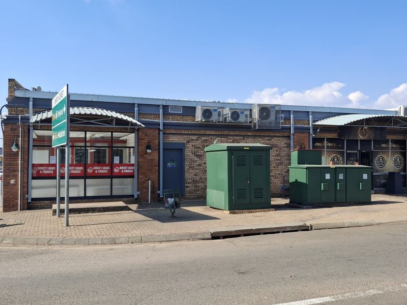 Street-level view of a commercial property featuring a brick facade, large storefront windows, metal awnings, and external utility infrastructure.
