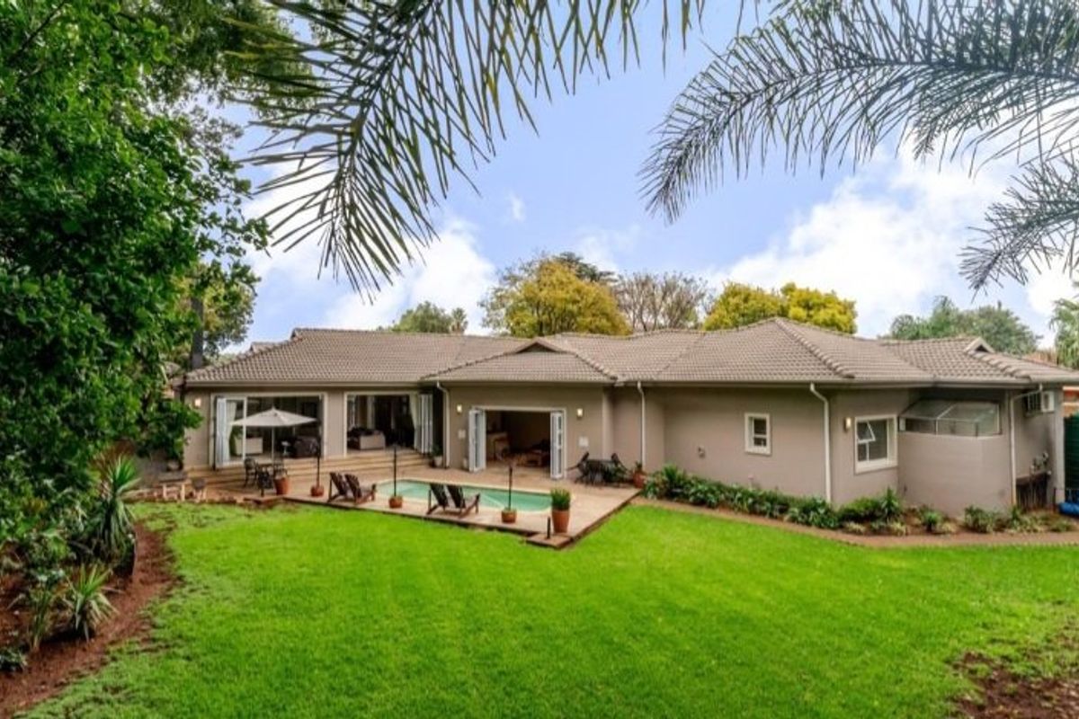 Spacious rear exterior view featuring a well-maintained garden, swimming pool, paved patio area, and bi-fold doors leading into the home.
