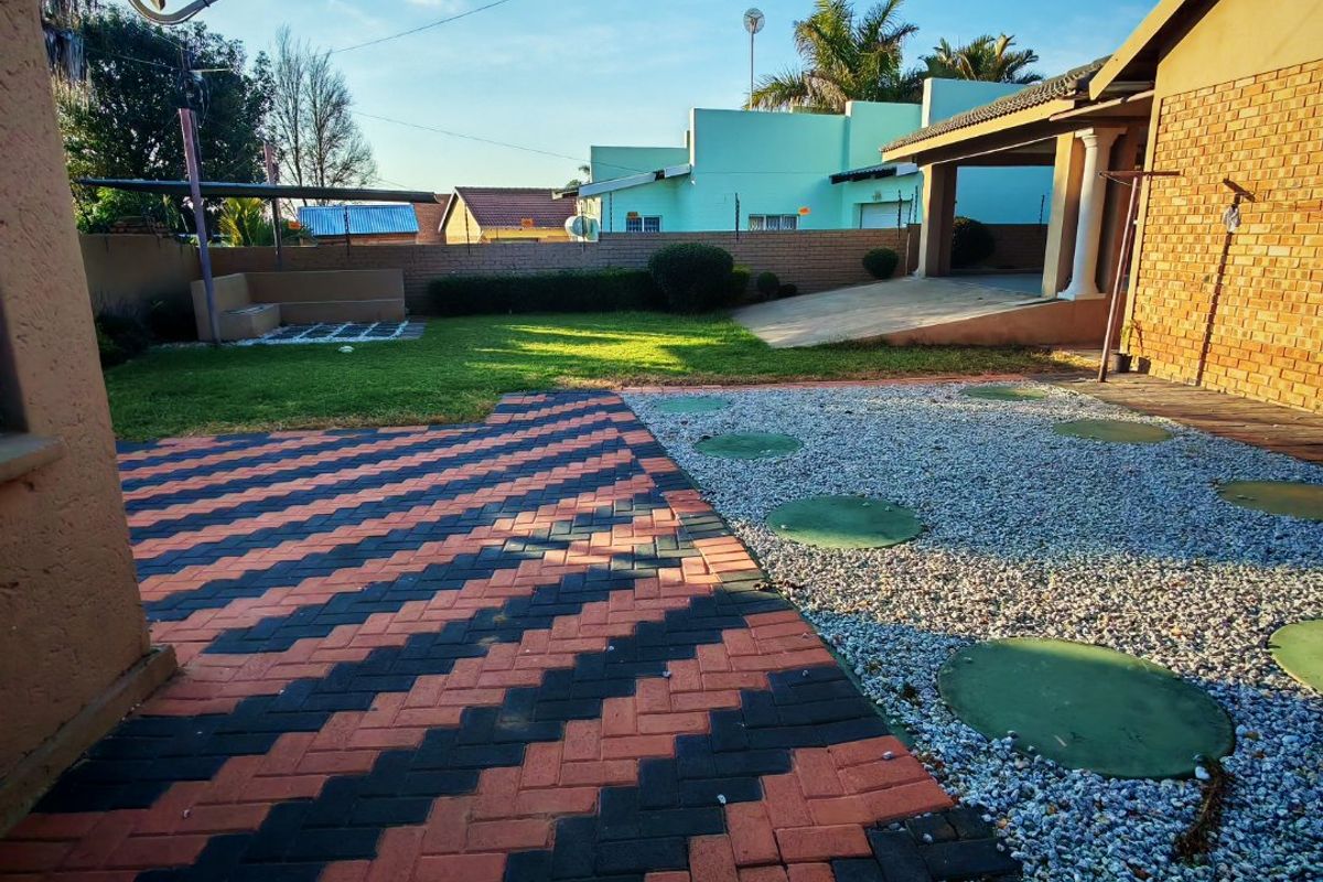 A well-maintained rear garden featuring a combination of patterned brick paving, gravel landscaping, a small lawn, and a covered patio area.